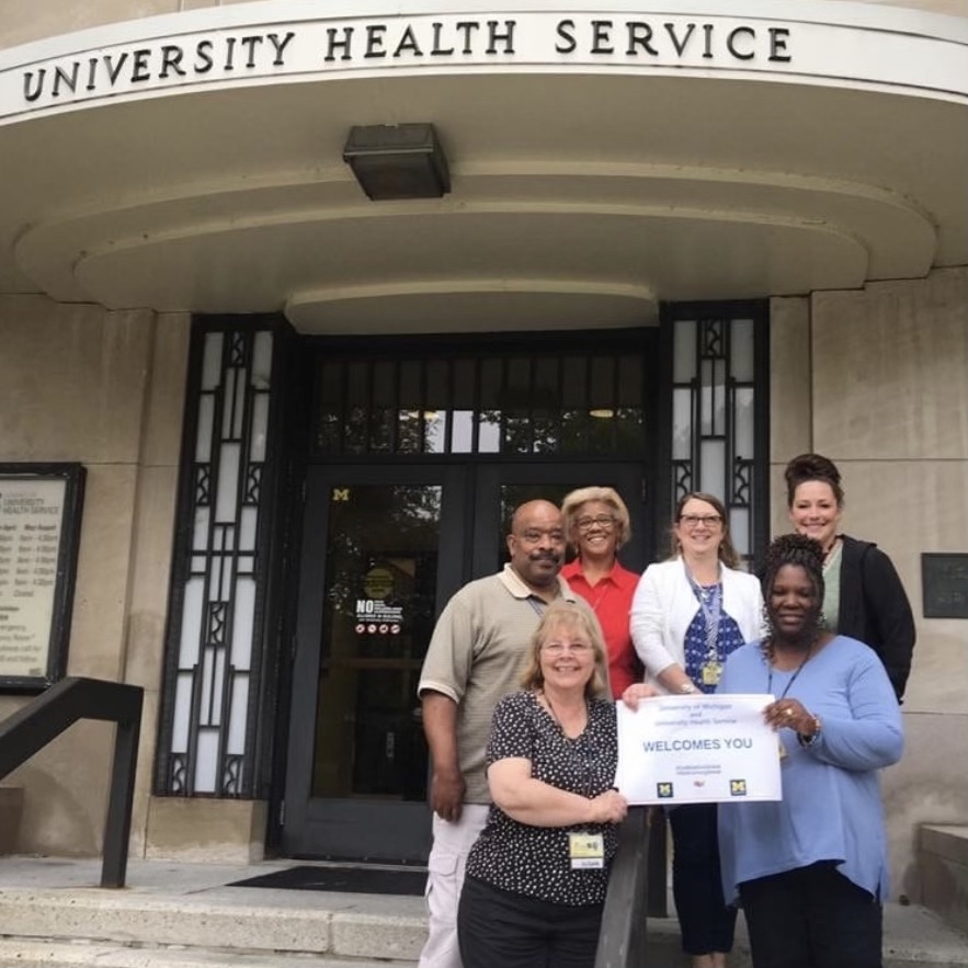 The University Health Service employees are posing with a 'Welcome You' sign.