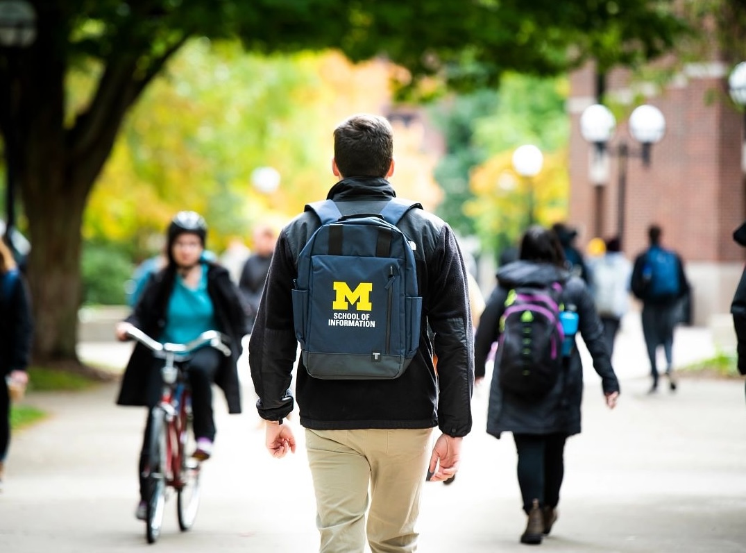 A student wears a UMSI backpack in fall on the drag.