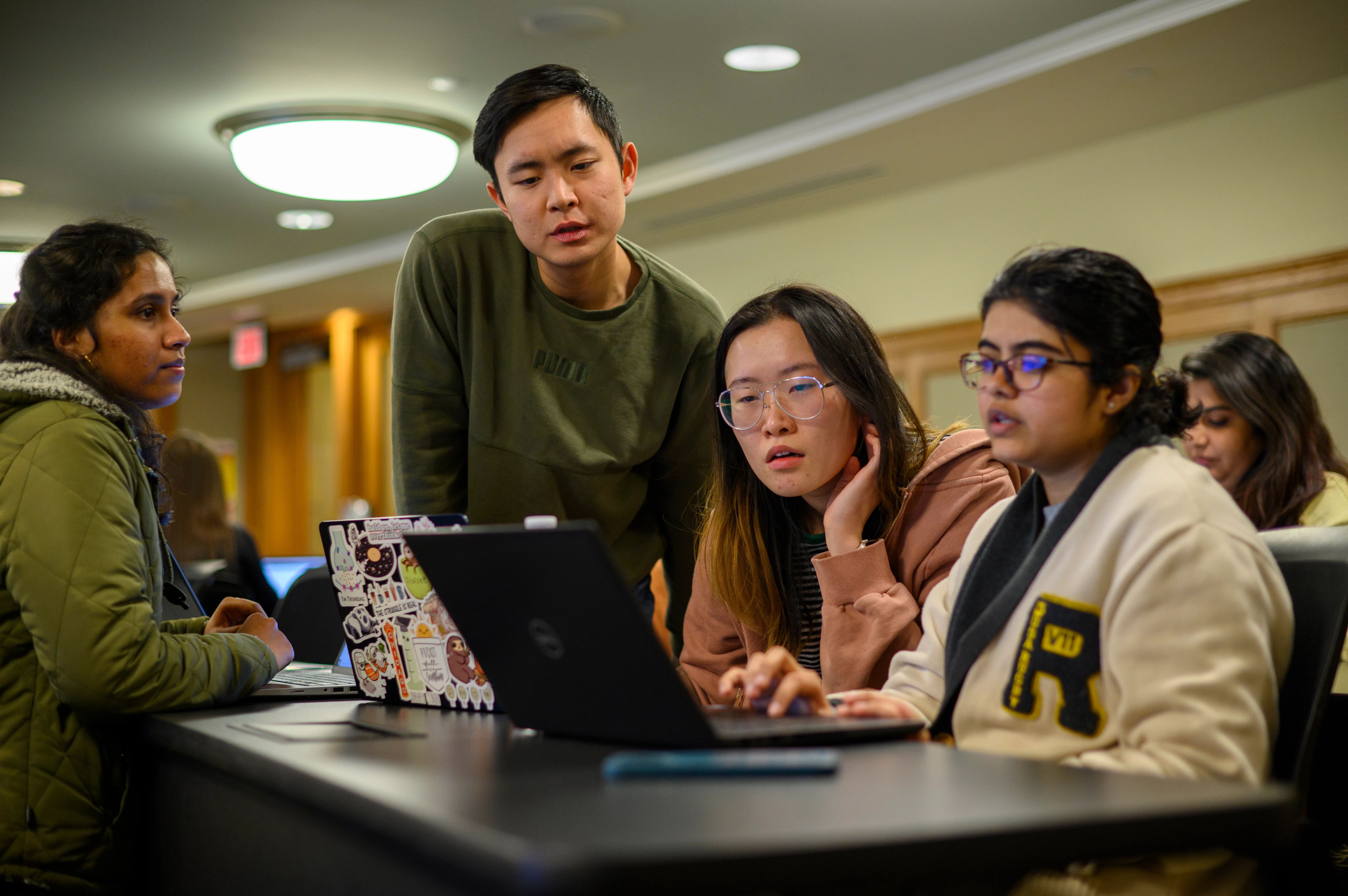 One student is instructing three other students on the laptop.
